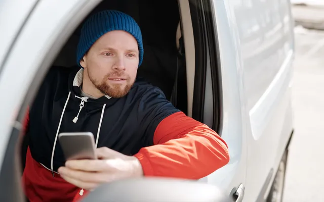 A contractor sitting in his work van, sending a message from his phone after finishing a job