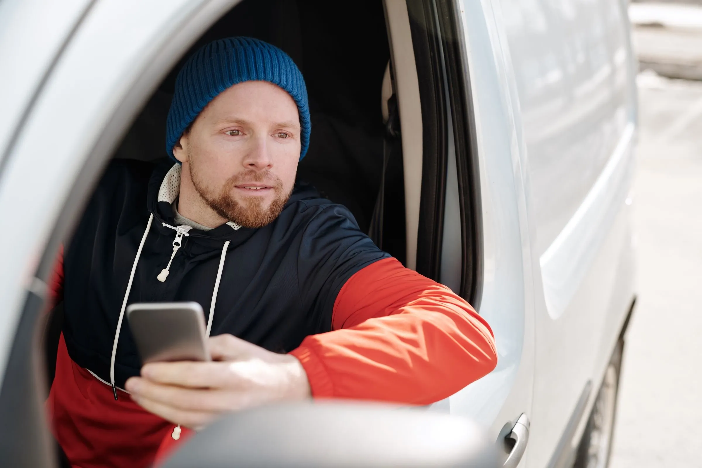 A contractor sitting in his work van, sending a message from his phone after finishing a job