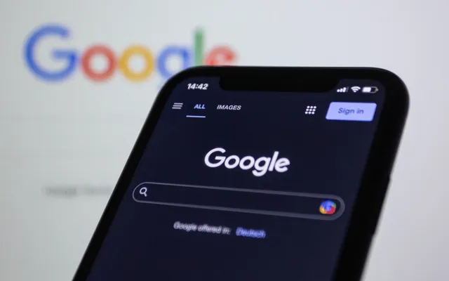 A phone showing the Google search box, held in front of a screen
