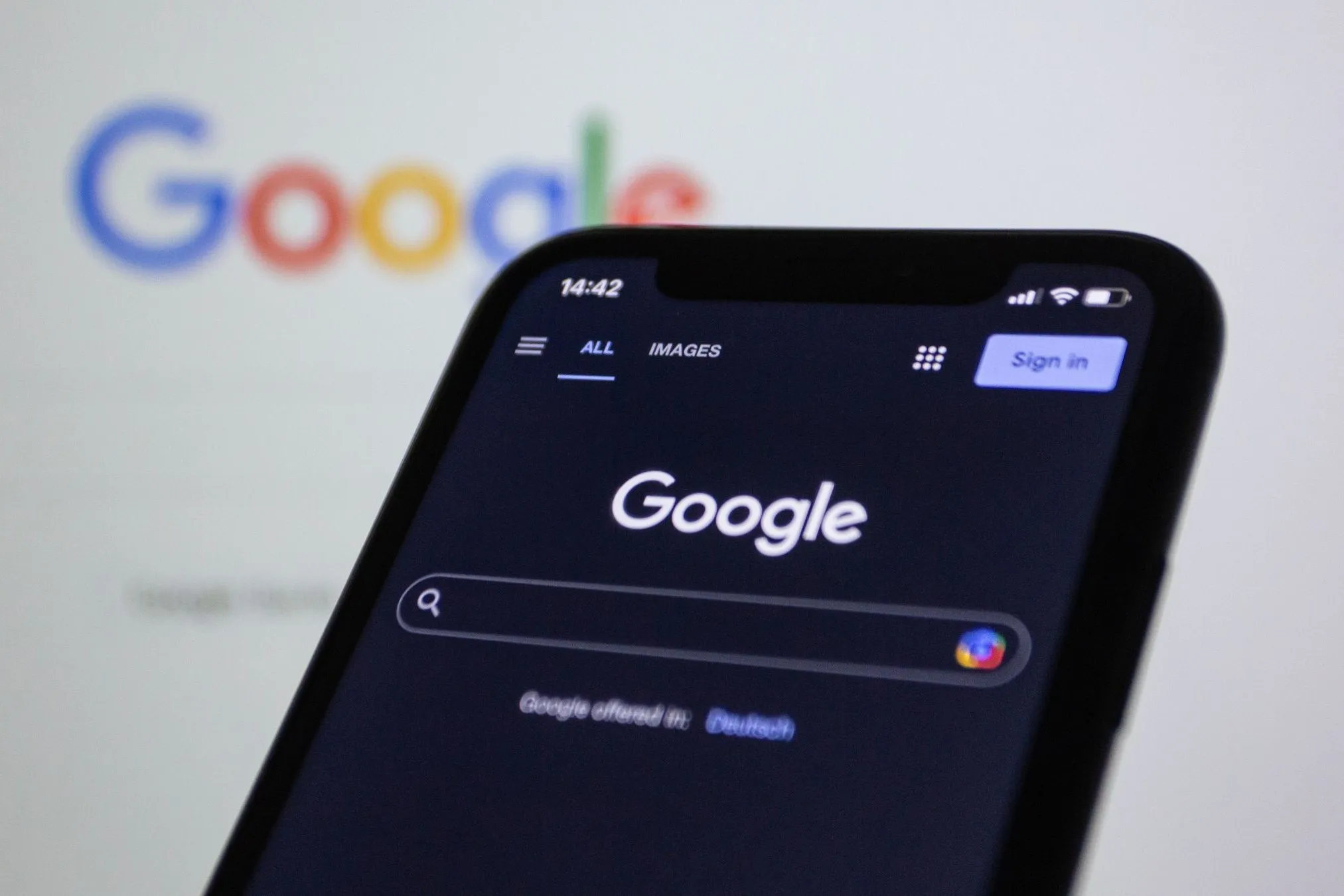 A phone showing the Google search box, held in front of a screen